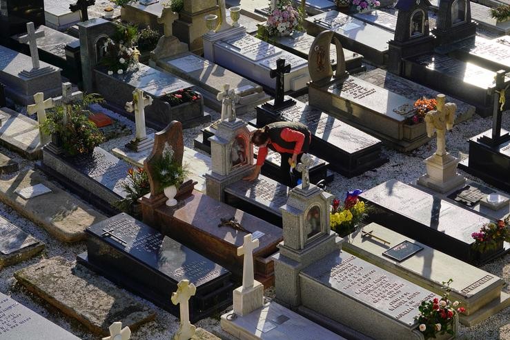 Unha muller limpa unha lápida do cemiterio de Quintana dos Mortos de Santa María A Nova, a 26 outubro de 2021, en Noia 