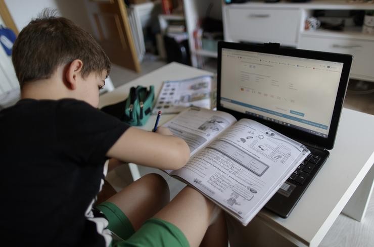 Un alumno de primaria fai os deberes da materia de Inglés con varios libros e un computador 