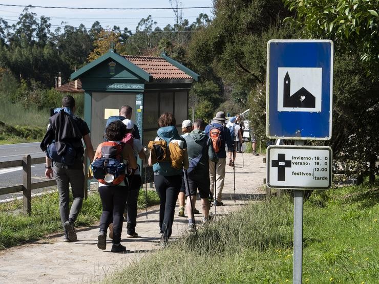 Un grupo de peregrinos pasa fronte a un cartel mentres realizan o Camiño de Santiago/ César Arxina