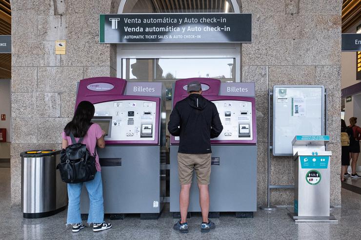 Dúas persoas compran billetes nos caixeiros de venda automática na estación de trens de Santiago de Compostela / César Arxina - Arquivo
