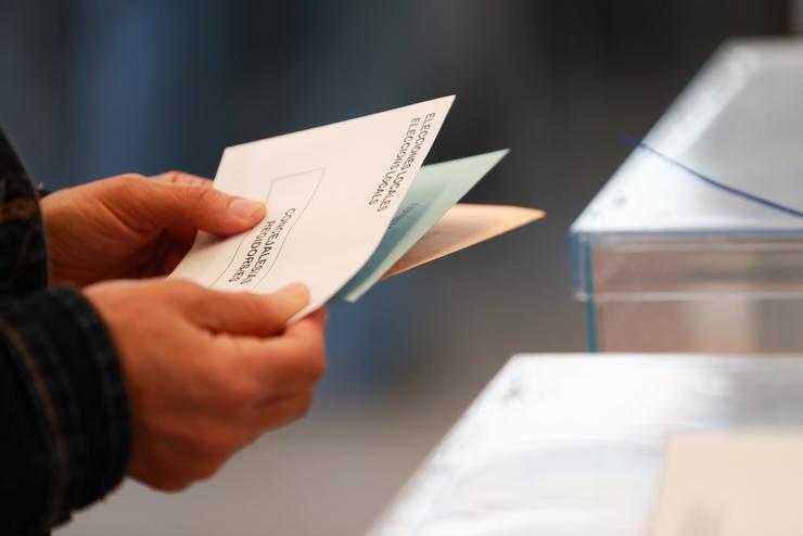 Unha persoa sostén papeletas electorais fronte ás urnas 