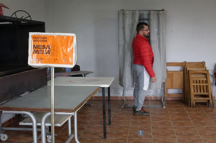 Unha persoa xunto a unha cabina electoral exerce o seu dereito a voto na mesa electoral do local parroquial de Recelle, nunha mesa que agrupa a varias aldeas da contorna, a 28 de maio de 2023, en Portomarín 