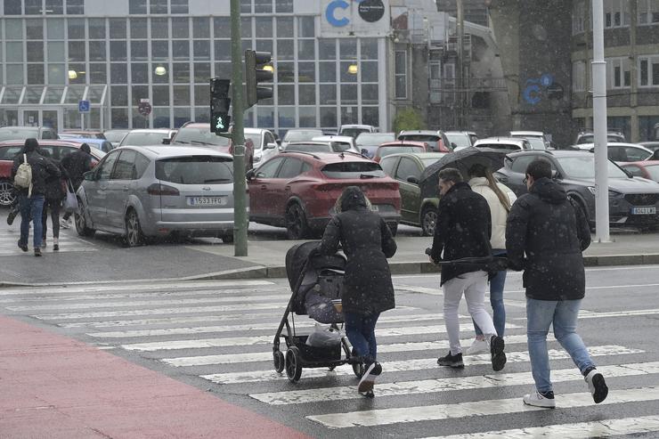 Varias persoas cruzan un paso de peóns tratando de refuxiarse da choiva na Coruña 