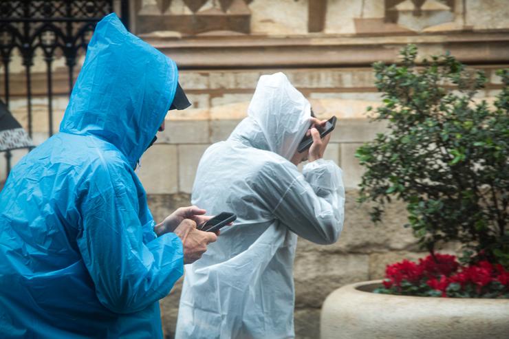 Dúas persoas protéxense da choiva cun impermeable 